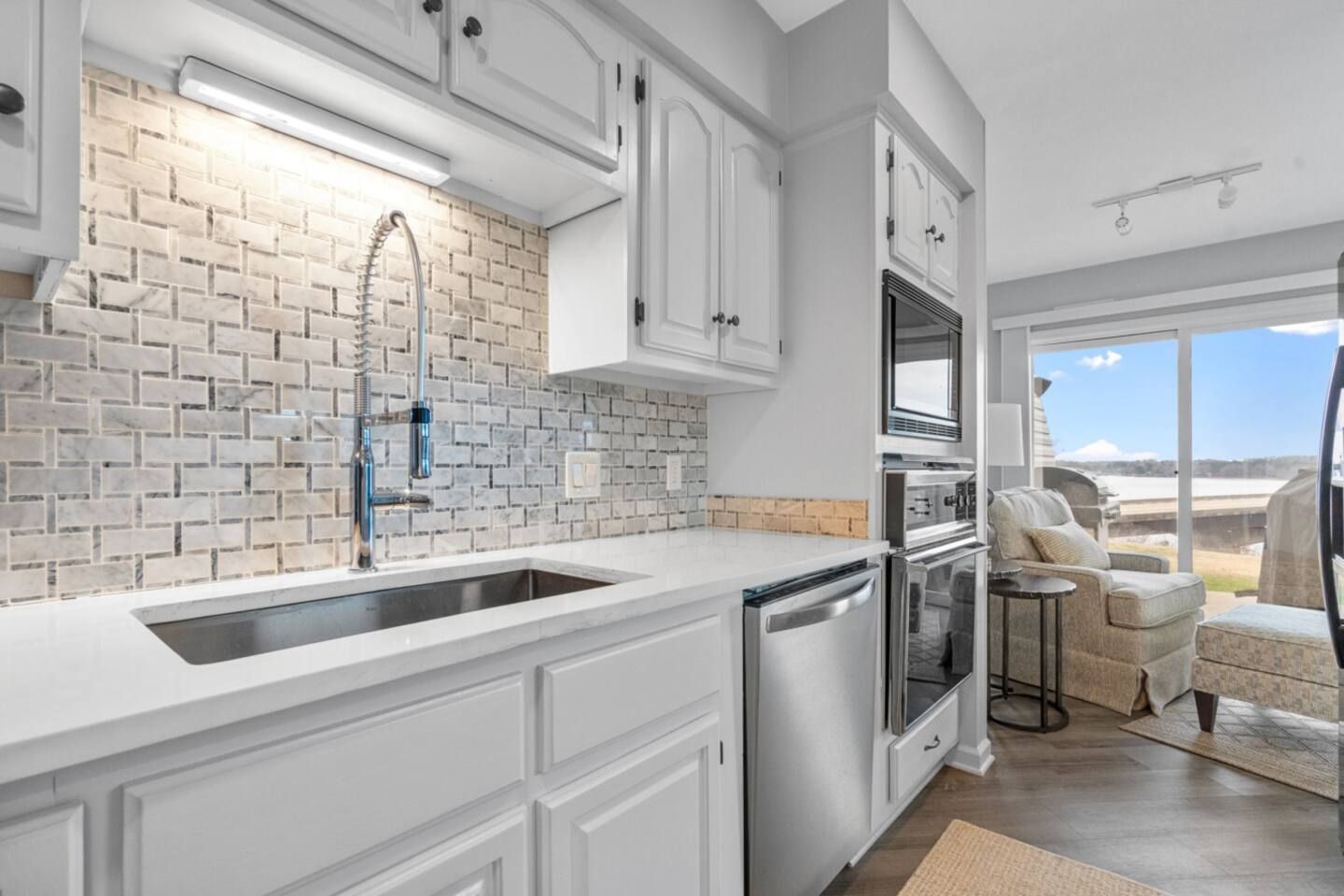 A kitchen with white cabinets , stainless steel appliances , a sink , and a sliding glass door.