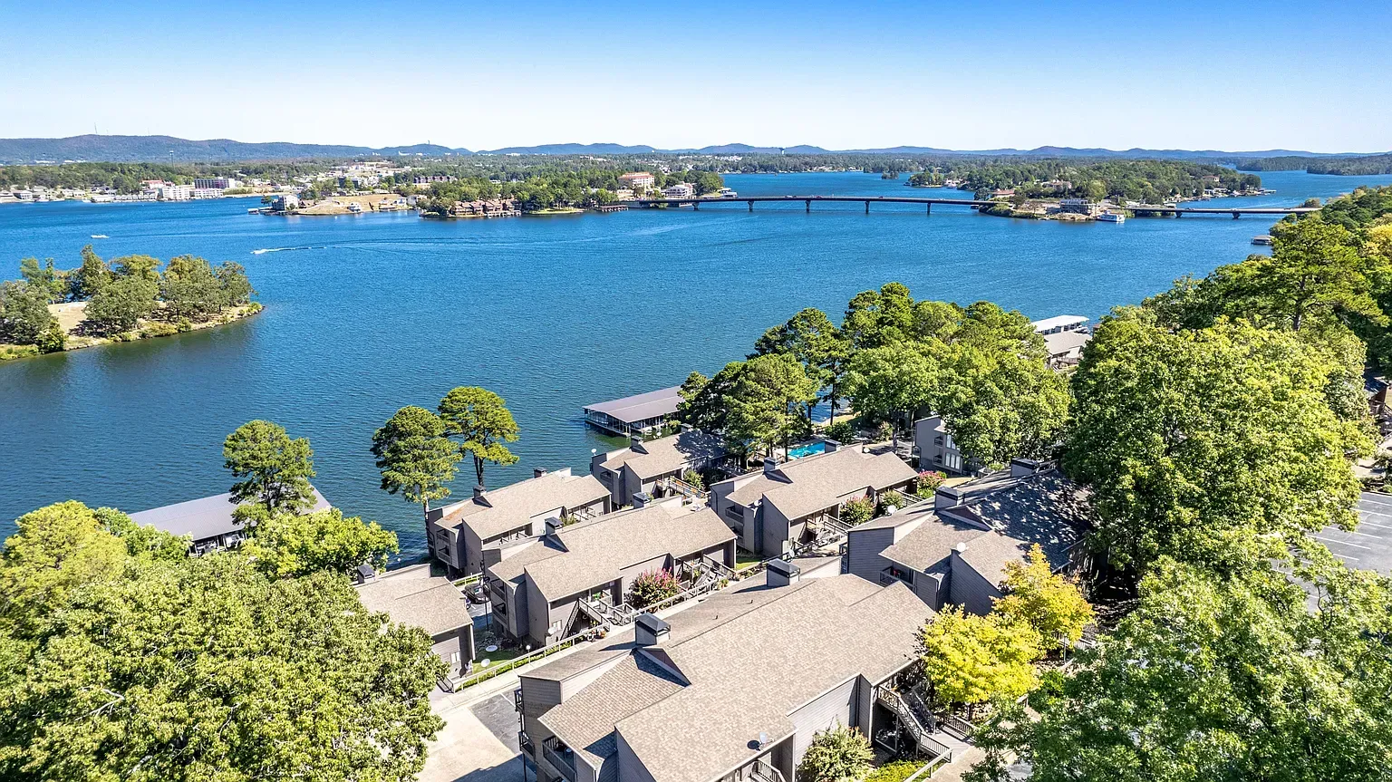 Aerial view of waterfront houses with docks, on a lake, with islands and a bridge in the distance.