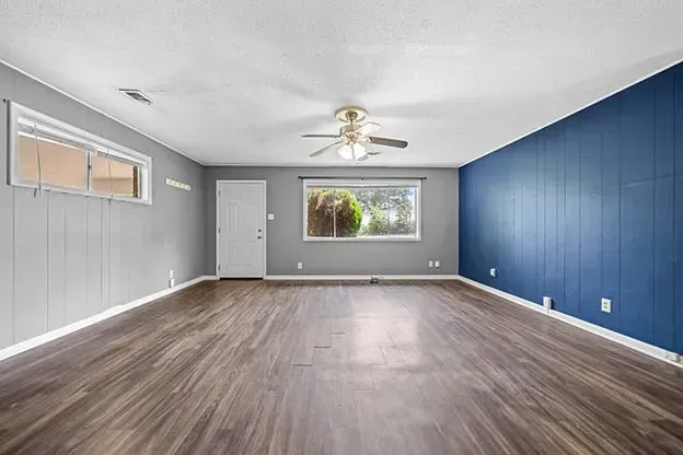 An empty living room with hardwood floors , blue walls and a ceiling fan.