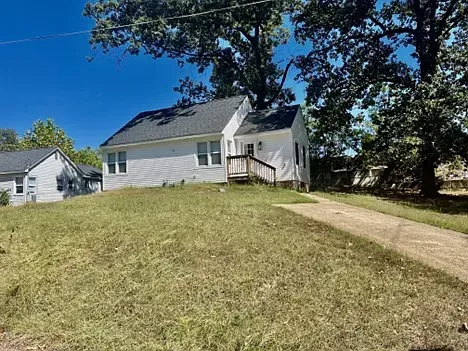 A small white house is sitting on top of a grassy hill next to a dirt road.