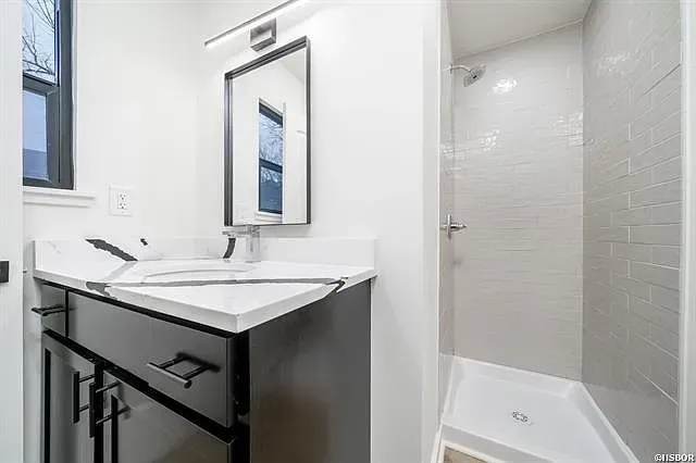 A bathroom with a sink , mirror , and shower stall.