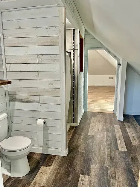 A bathroom with a toilet , sink , and wooden floor.