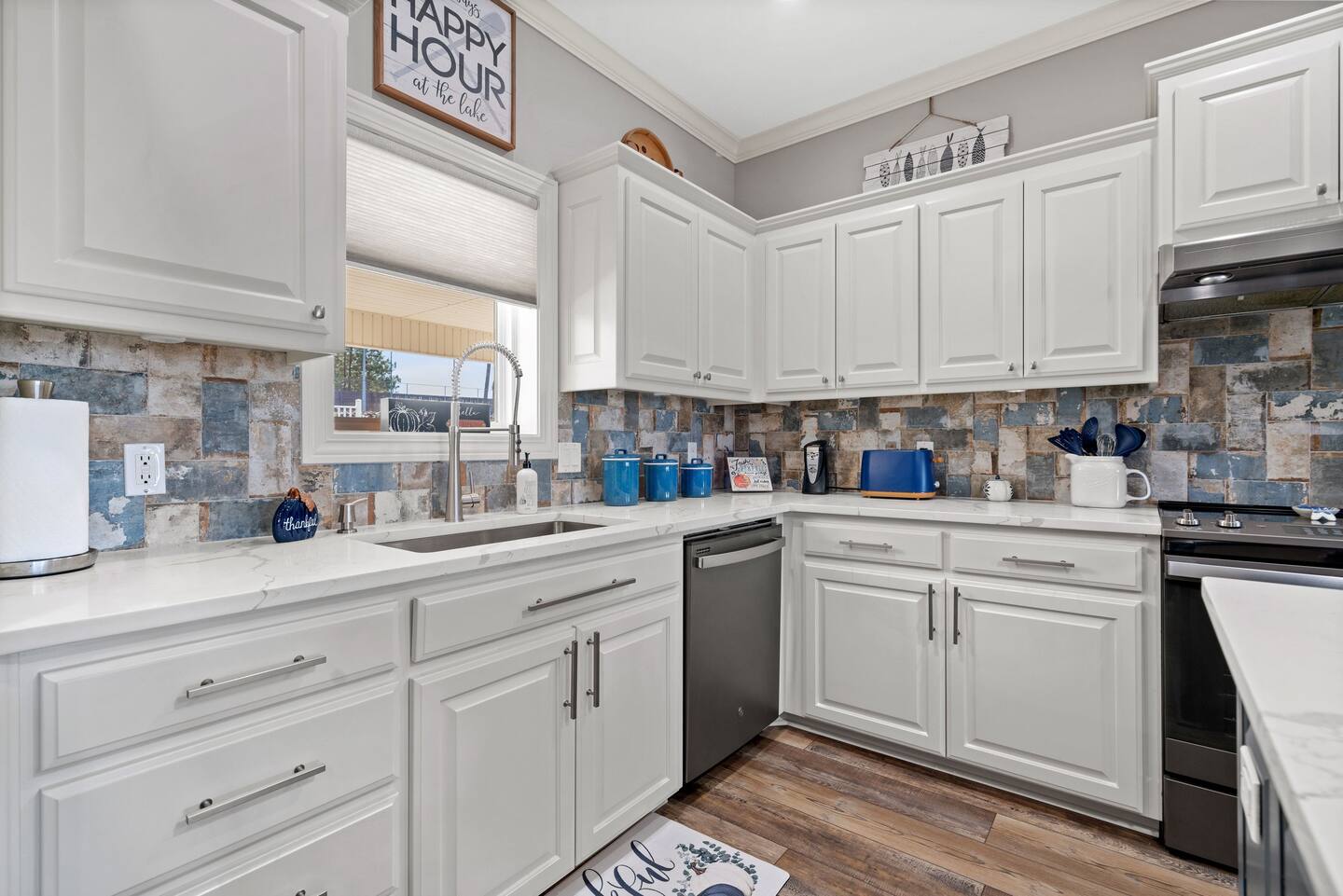 A kitchen with white cabinets , stainless steel appliances , a sink , and a window.