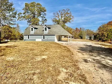 A house is sitting on top of a dry grass field next to a dirt road.