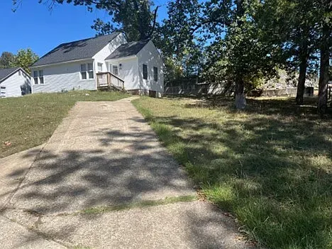 A white house is sitting on top of a grassy hill next to a driveway.