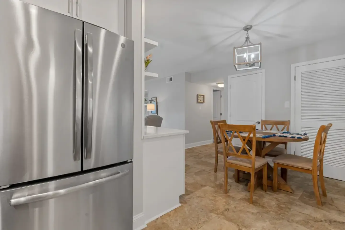 A stainless steel refrigerator is in a kitchen next to a dining room table and chairs.