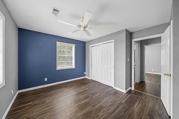 An empty bedroom with blue walls and hardwood floors and a ceiling fan.