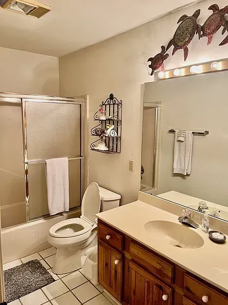Bathroom with a toilet, sink, and shower. Tan walls, brown vanity, and a few sea turtle decorations above the mirror.