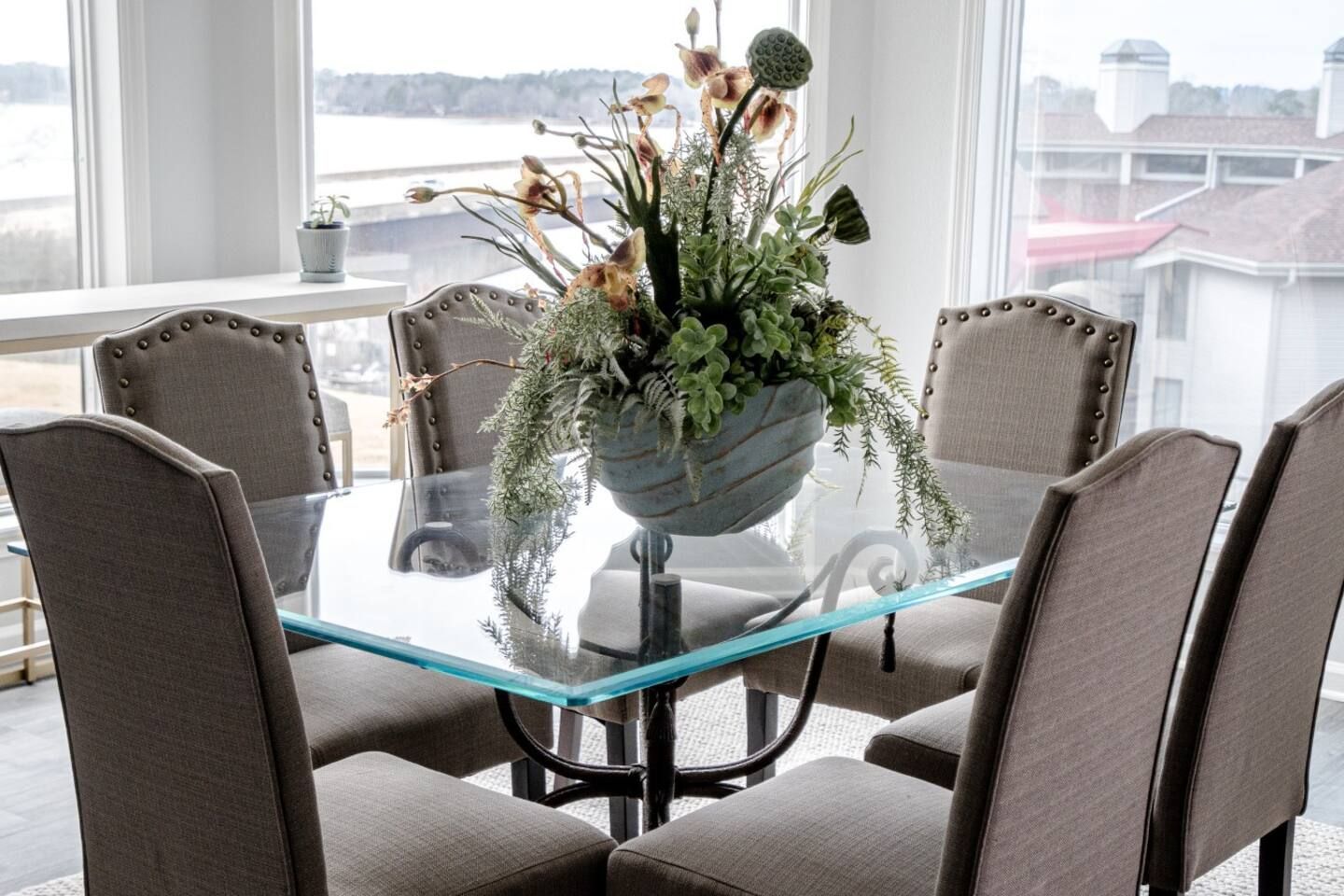 A dining room with a glass table and chairs and a vase of flowers on it.