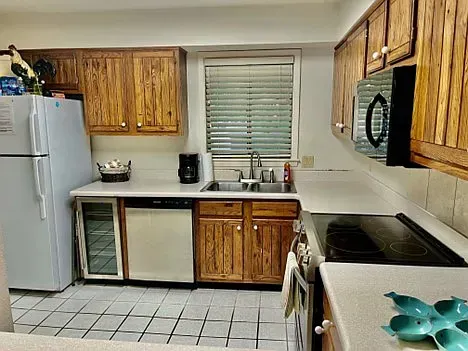 Kitchen with light-colored countertops, wood cabinets, white appliances, and a window with blinds.