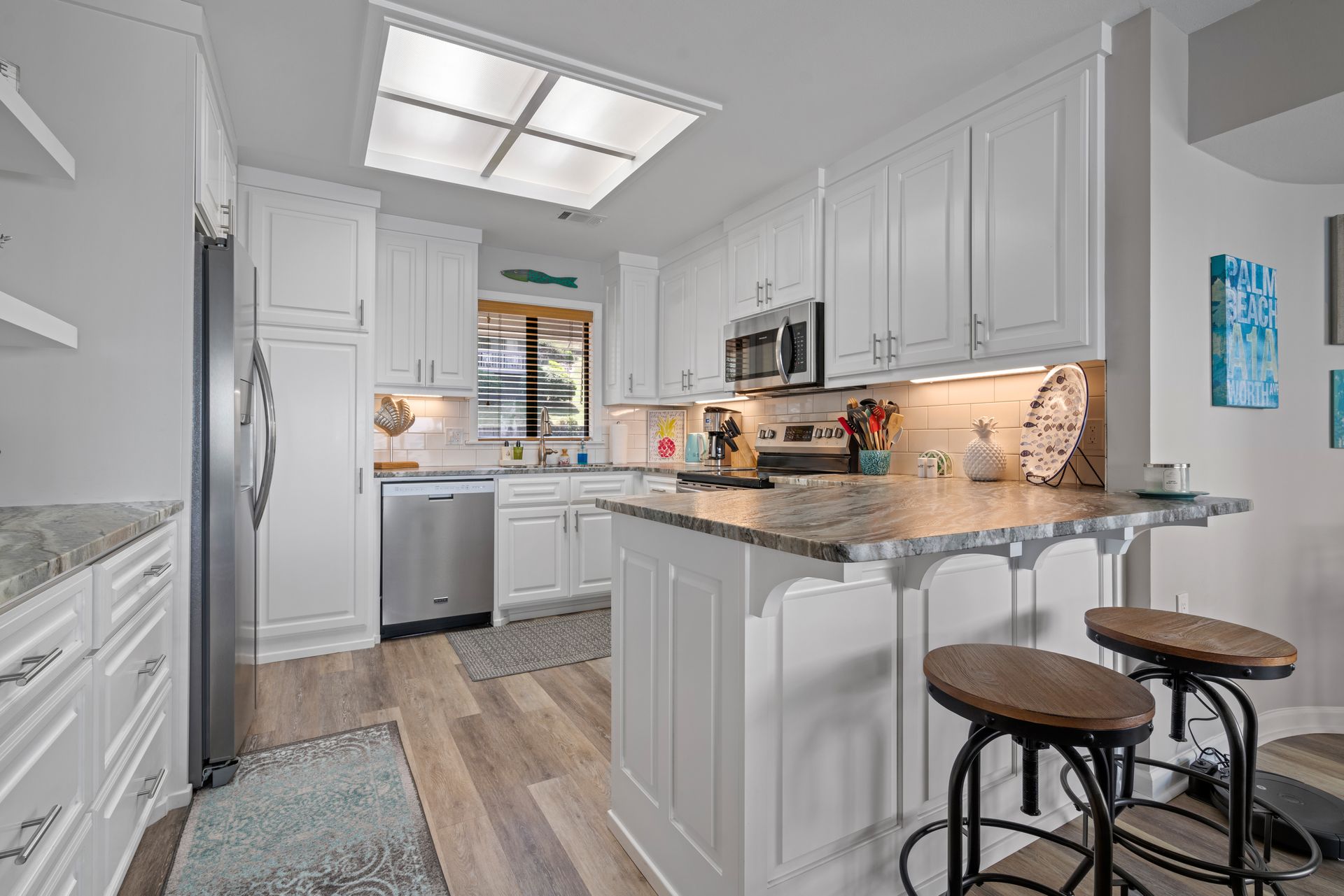 A kitchen with white cabinets , granite counter tops , stainless steel appliances and a large island.