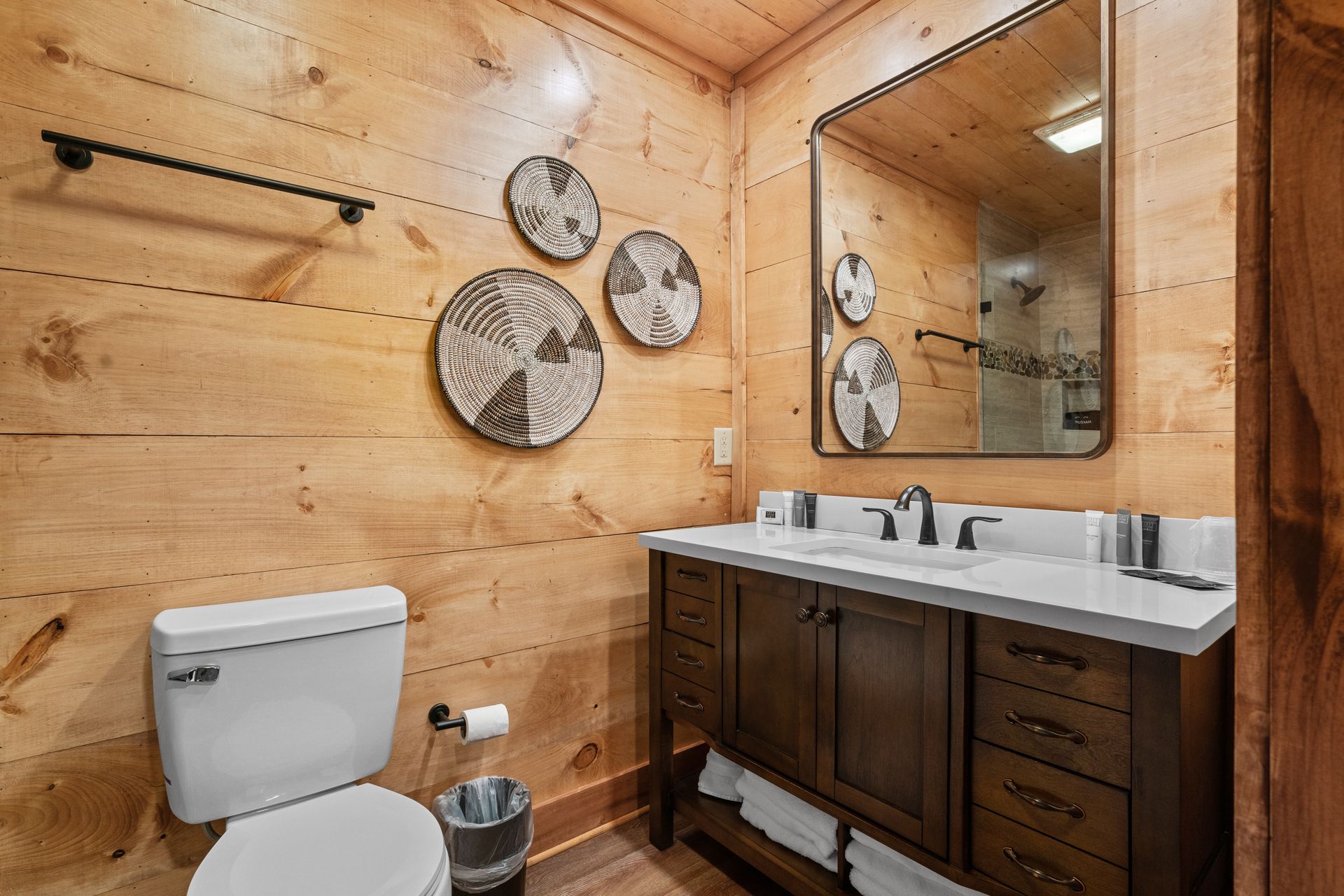 A bathroom with a toilet , sink , mirror and wooden walls.