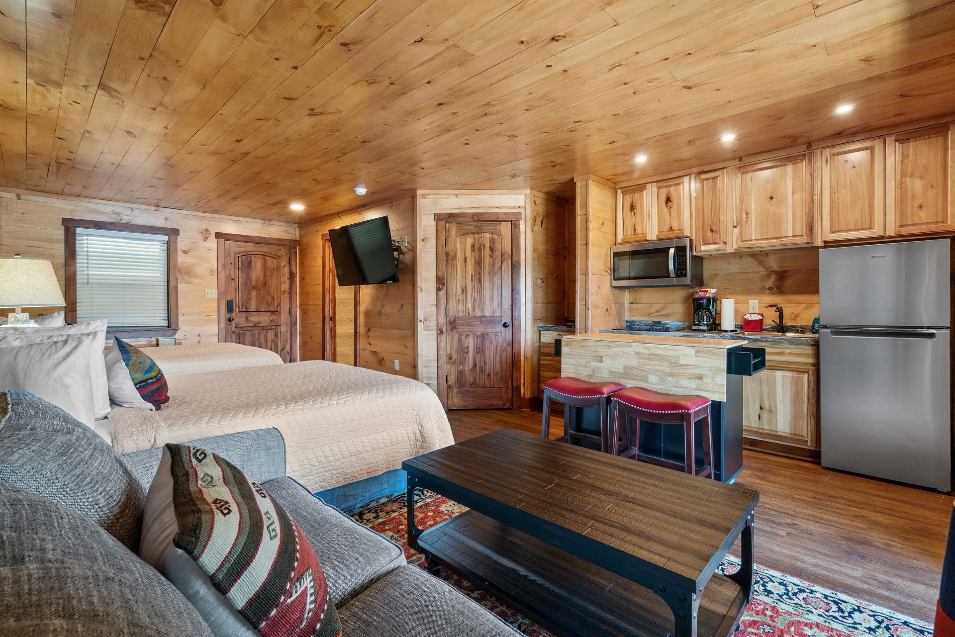 A living room with two beds , a couch , a table and a refrigerator.