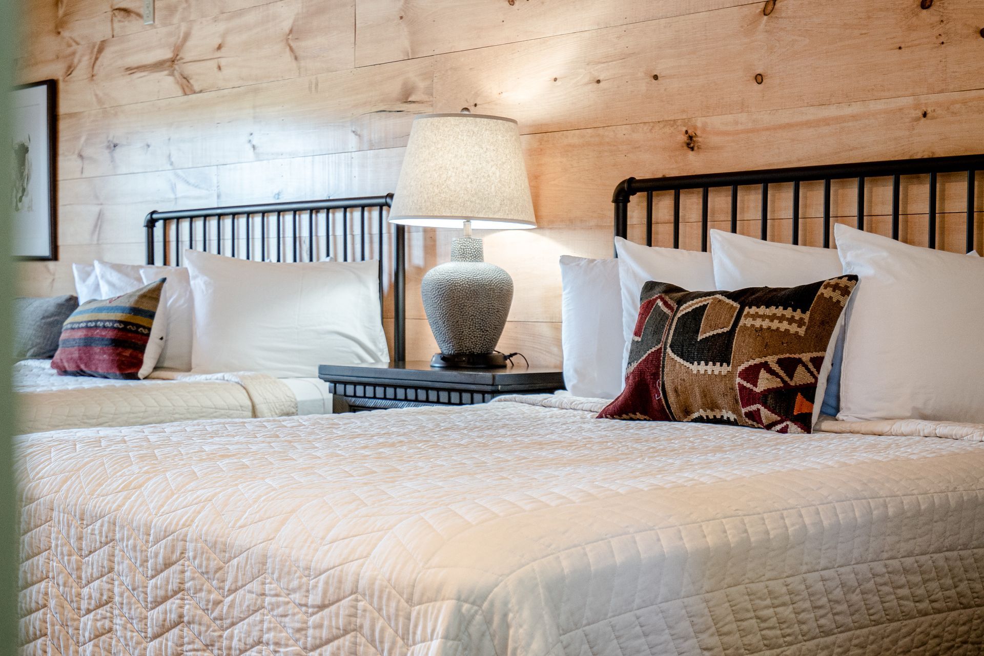 A bedroom with two beds , a lamp , and a wooden wall.