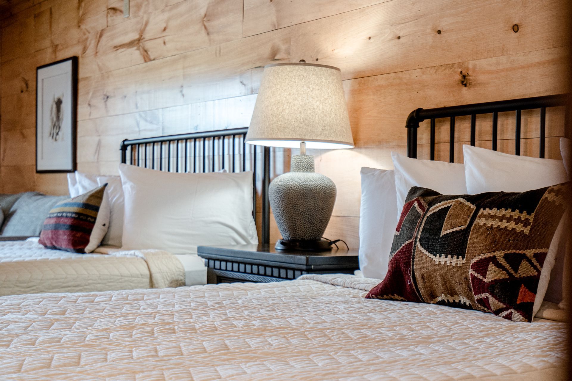 A bedroom with two beds , two lamps , and a wooden wall.