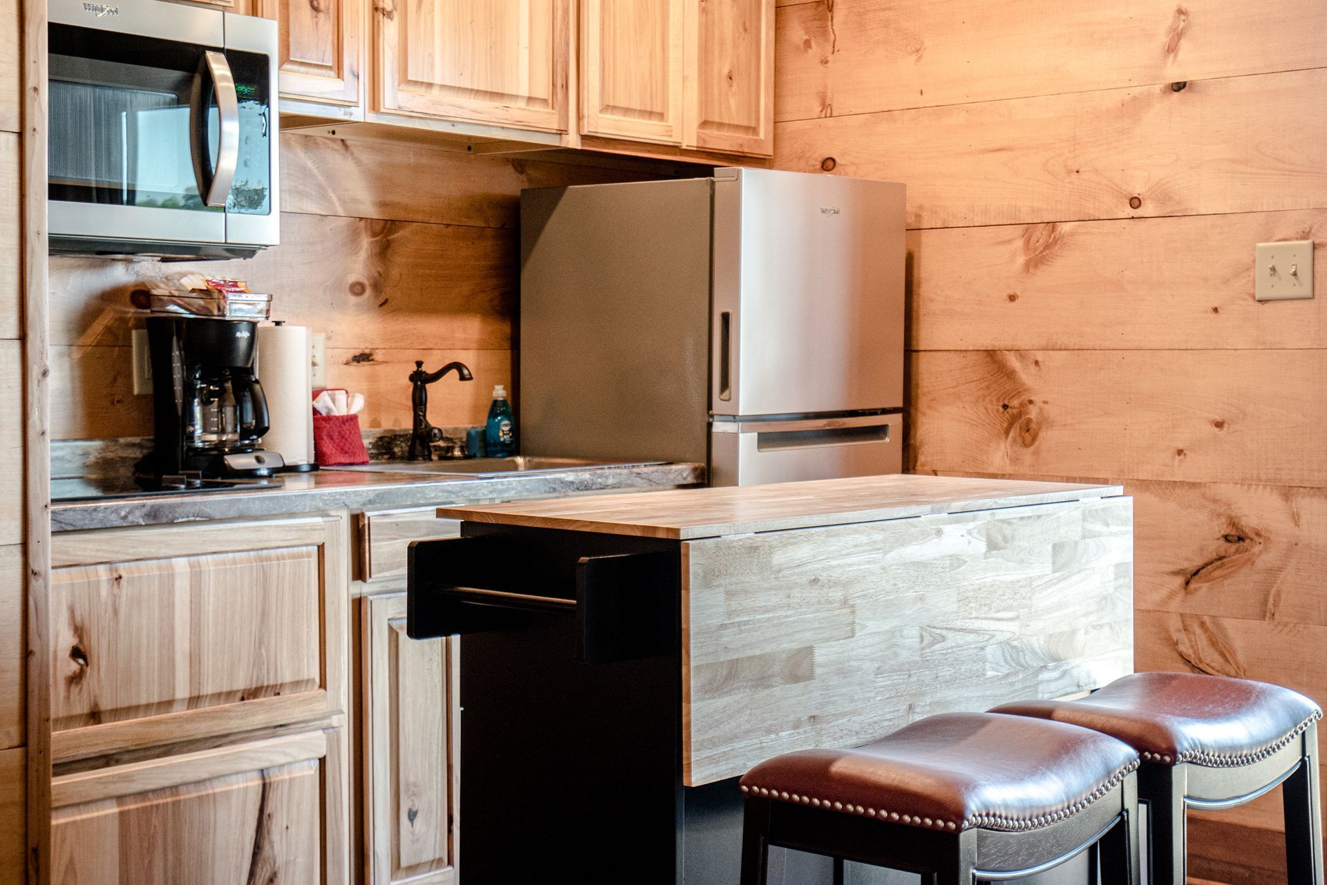 A kitchen in a log cabin with a refrigerator , microwave , sink , and bar.