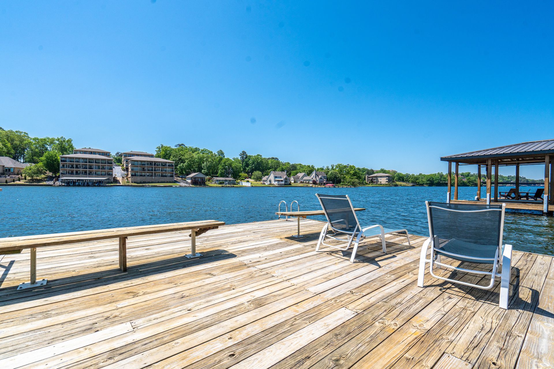 A wooden dock with chairs and a bench overlooking a lake.