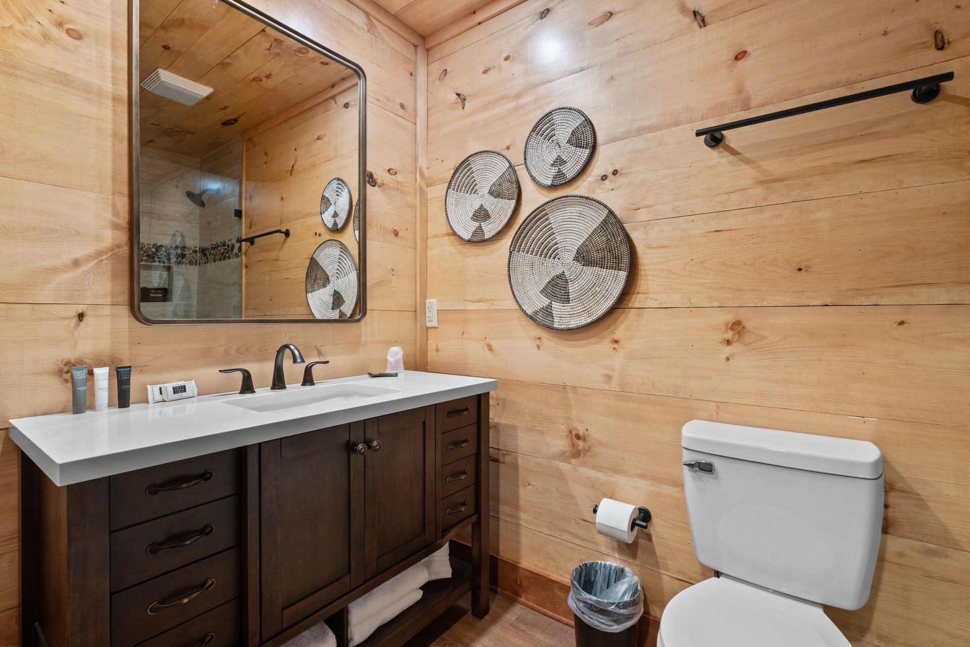 A bathroom with a sink , toilet , mirror and wooden walls.