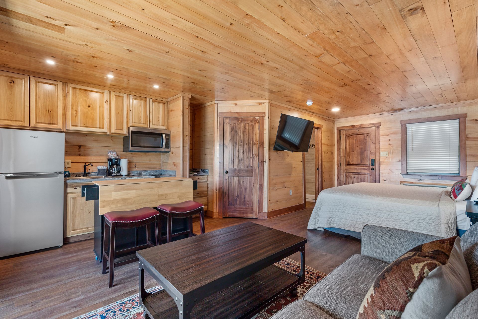 A living room with a couch , coffee table , and bed in a cabin.