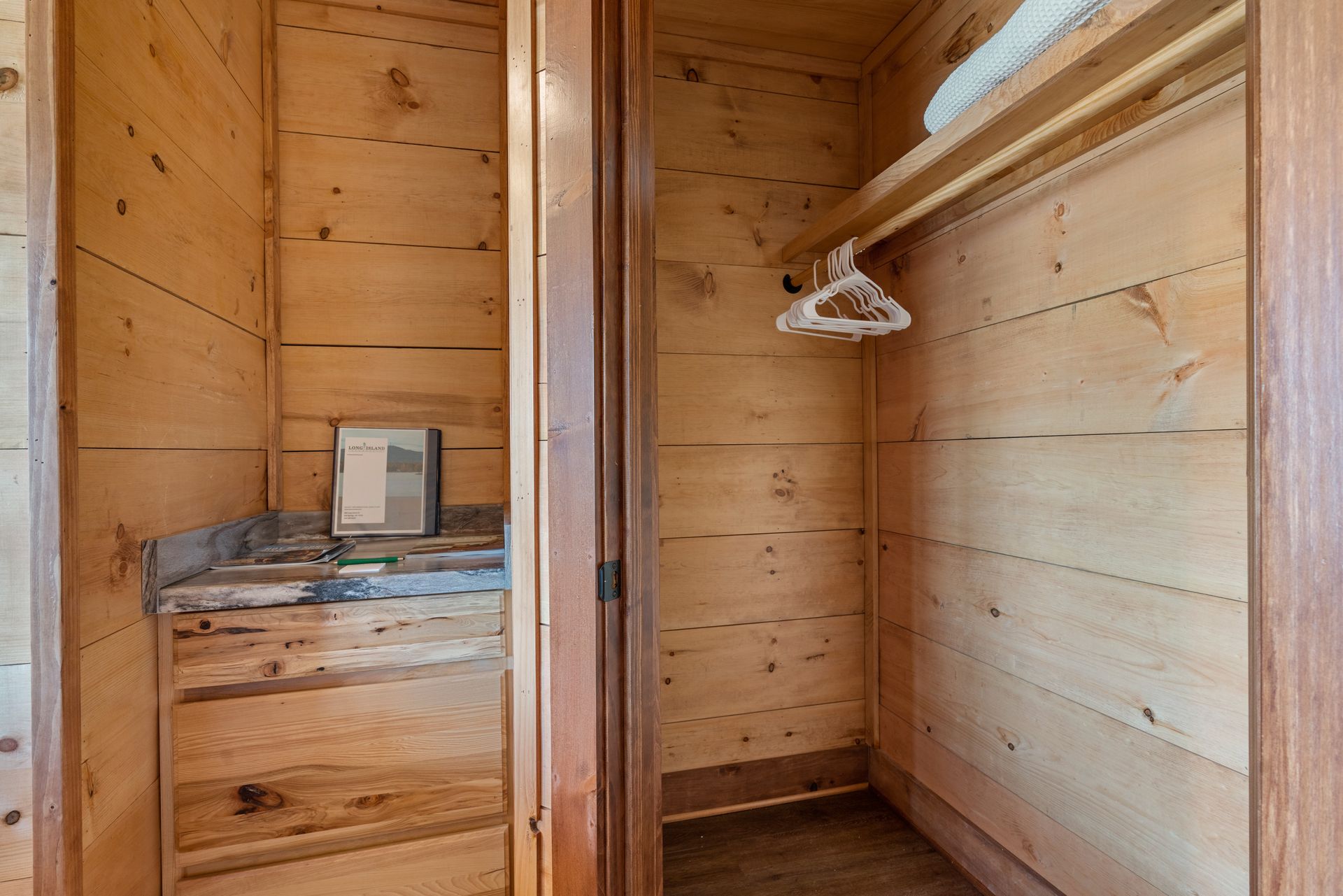 A wooden walk in closet with a mirror and clothes hanging on the wall.