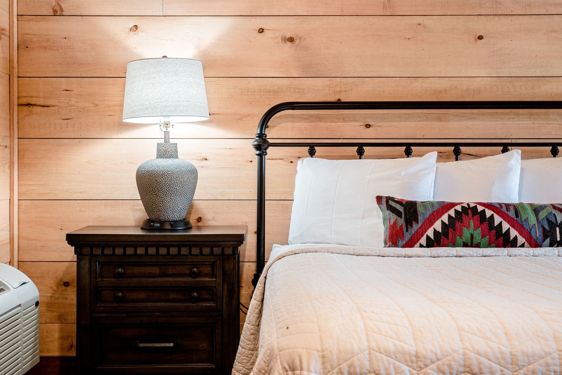 A bedroom with a bed , nightstand , lamp and wooden walls.