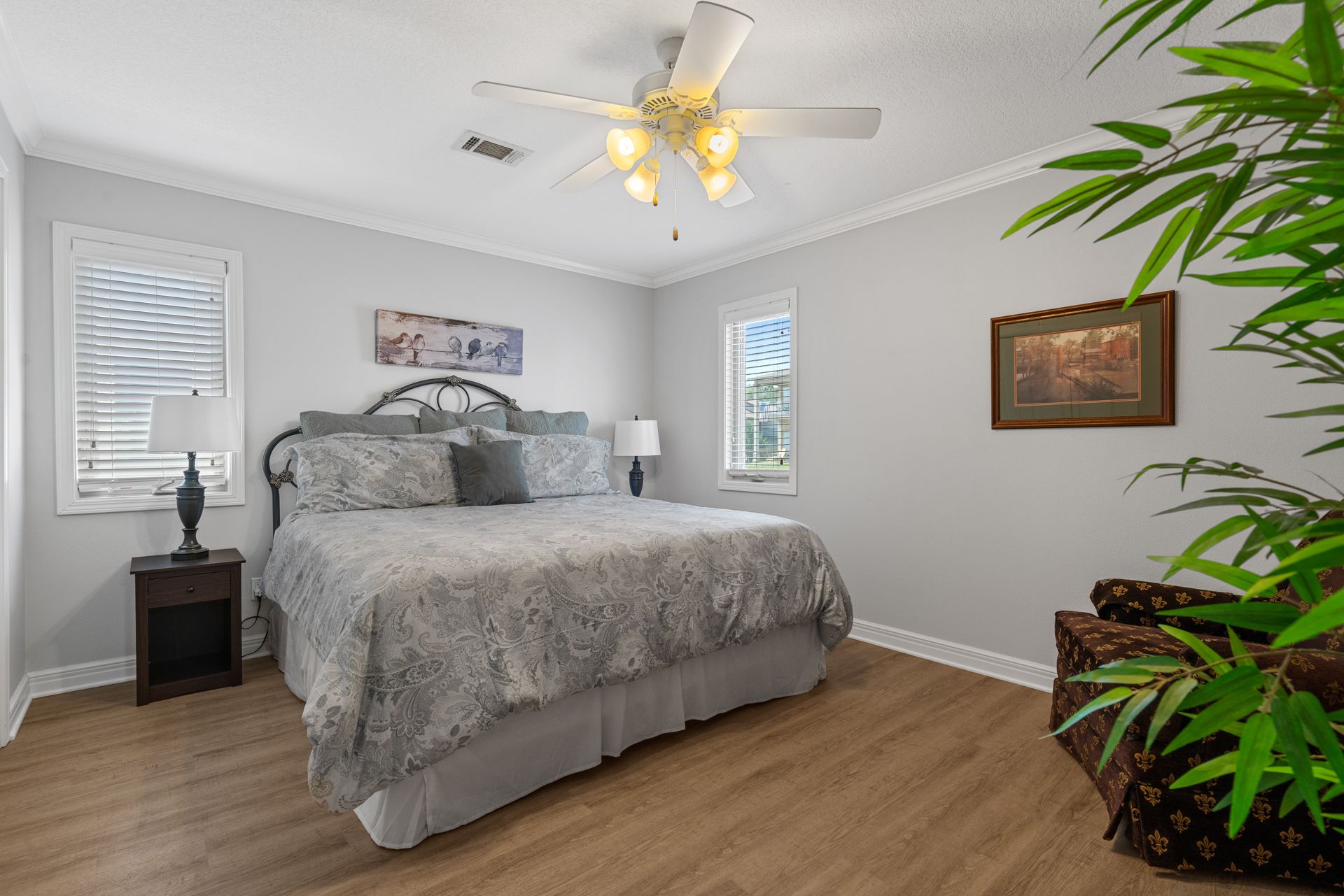 A bedroom with a king size bed , nightstand , chair and ceiling fan.