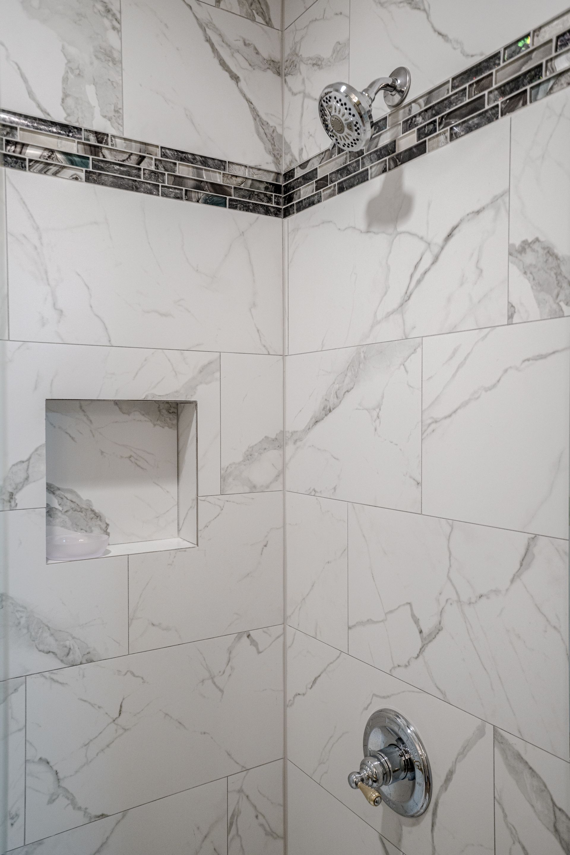 A close up of a shower with marble tiles and a shower head.