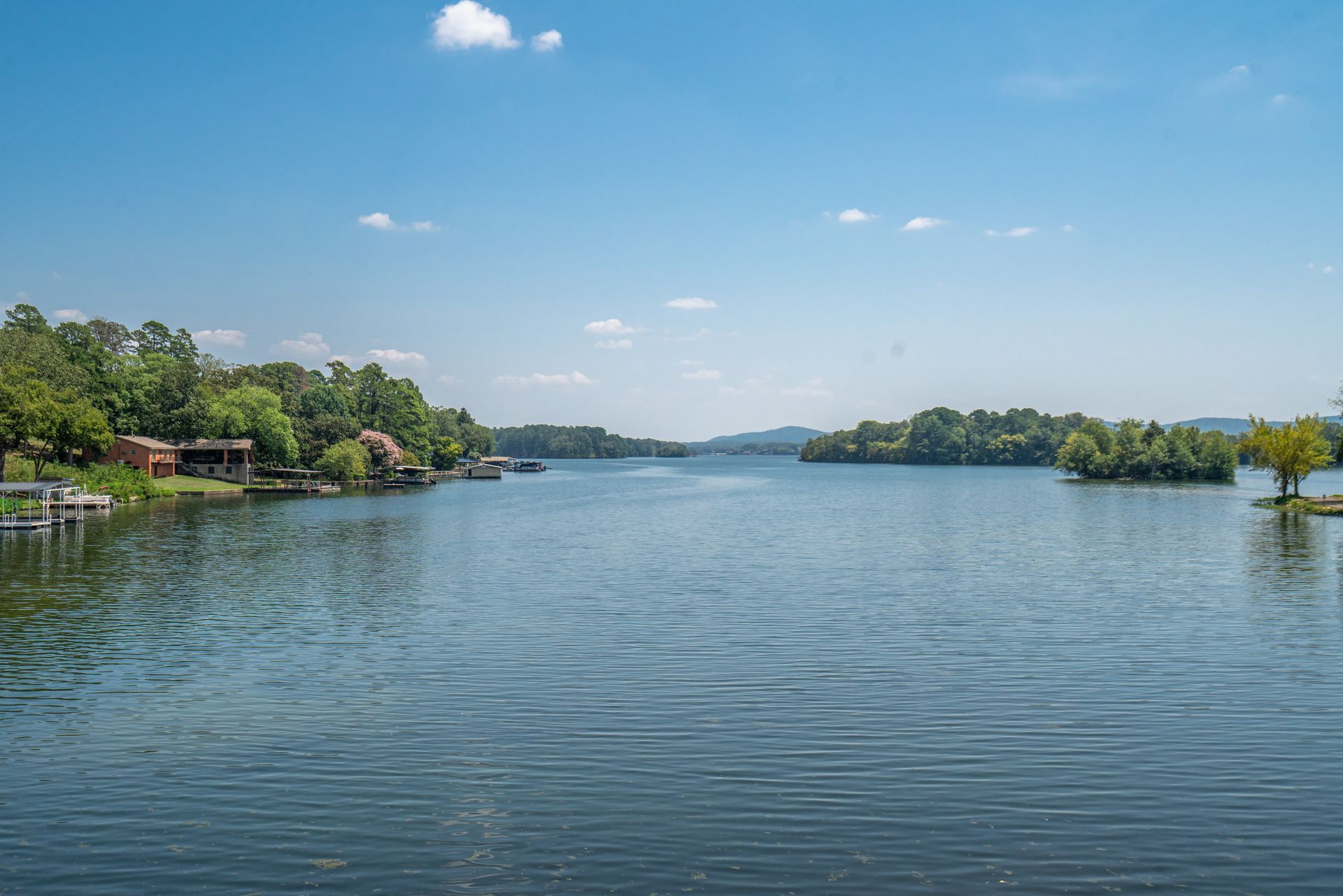 A large body of water surrounded by trees and houses on a sunny day.