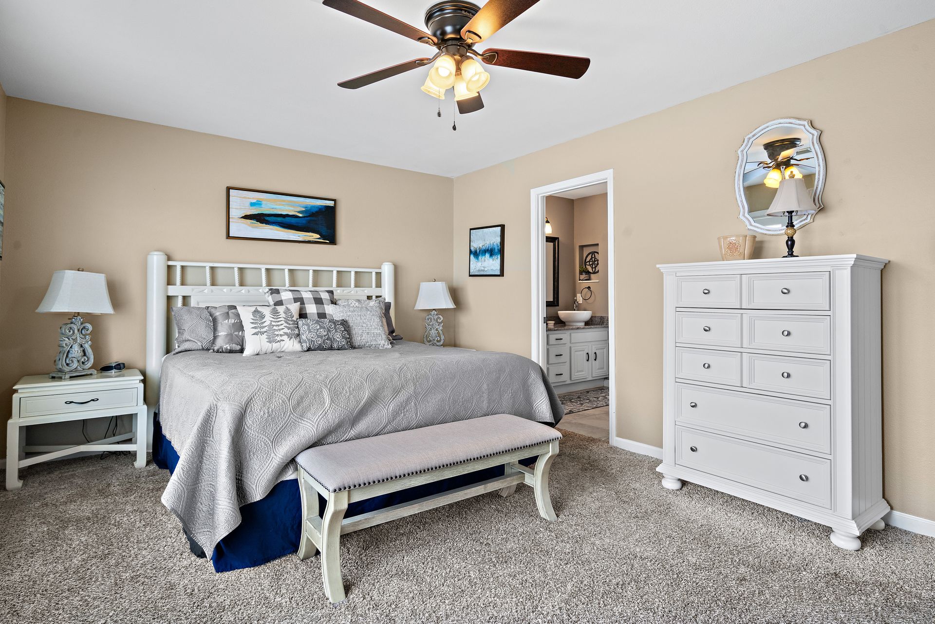 A bedroom with a king size bed , dresser , mirror and ceiling fan.