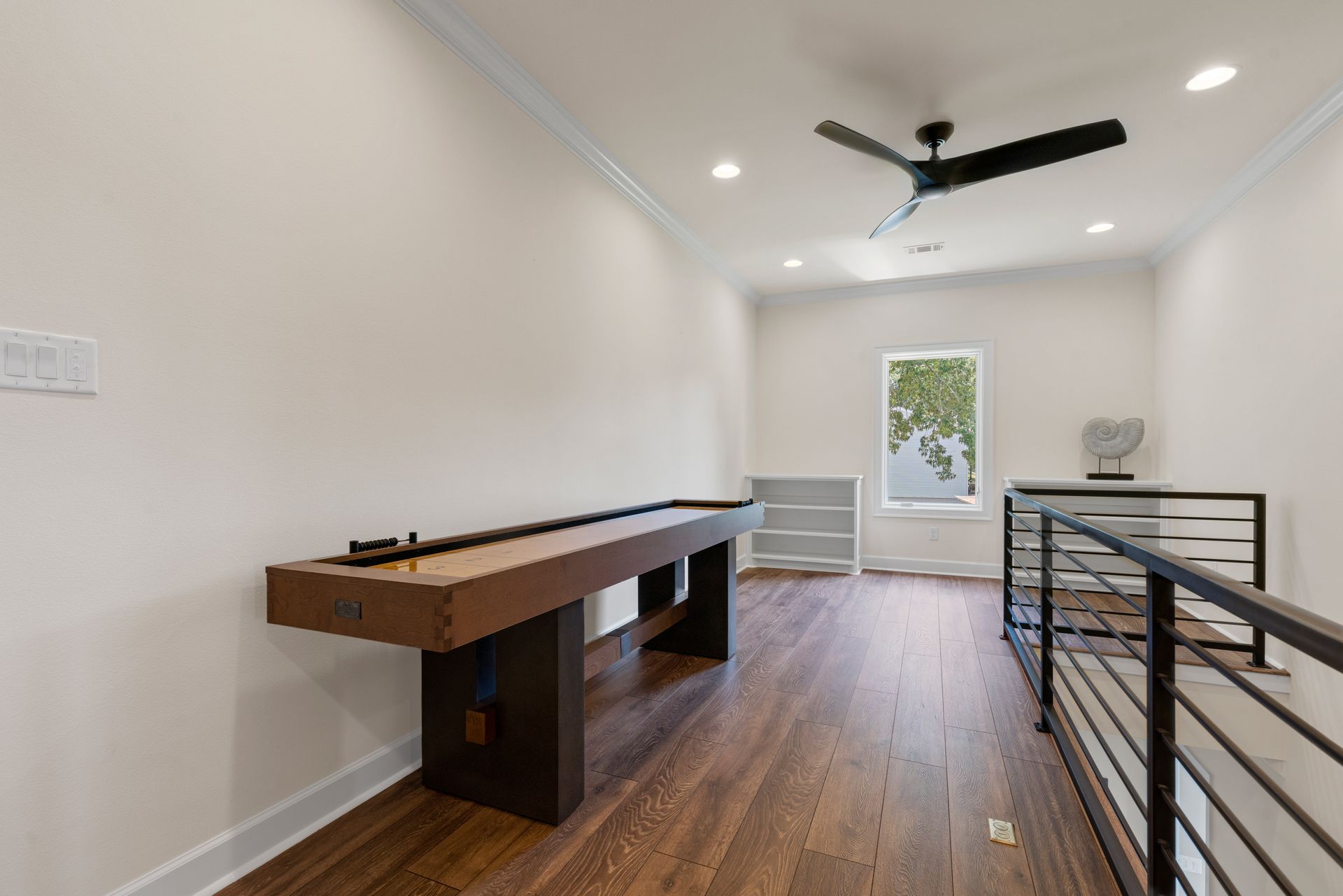 A game room with a shuffleboard table and a ceiling fan.