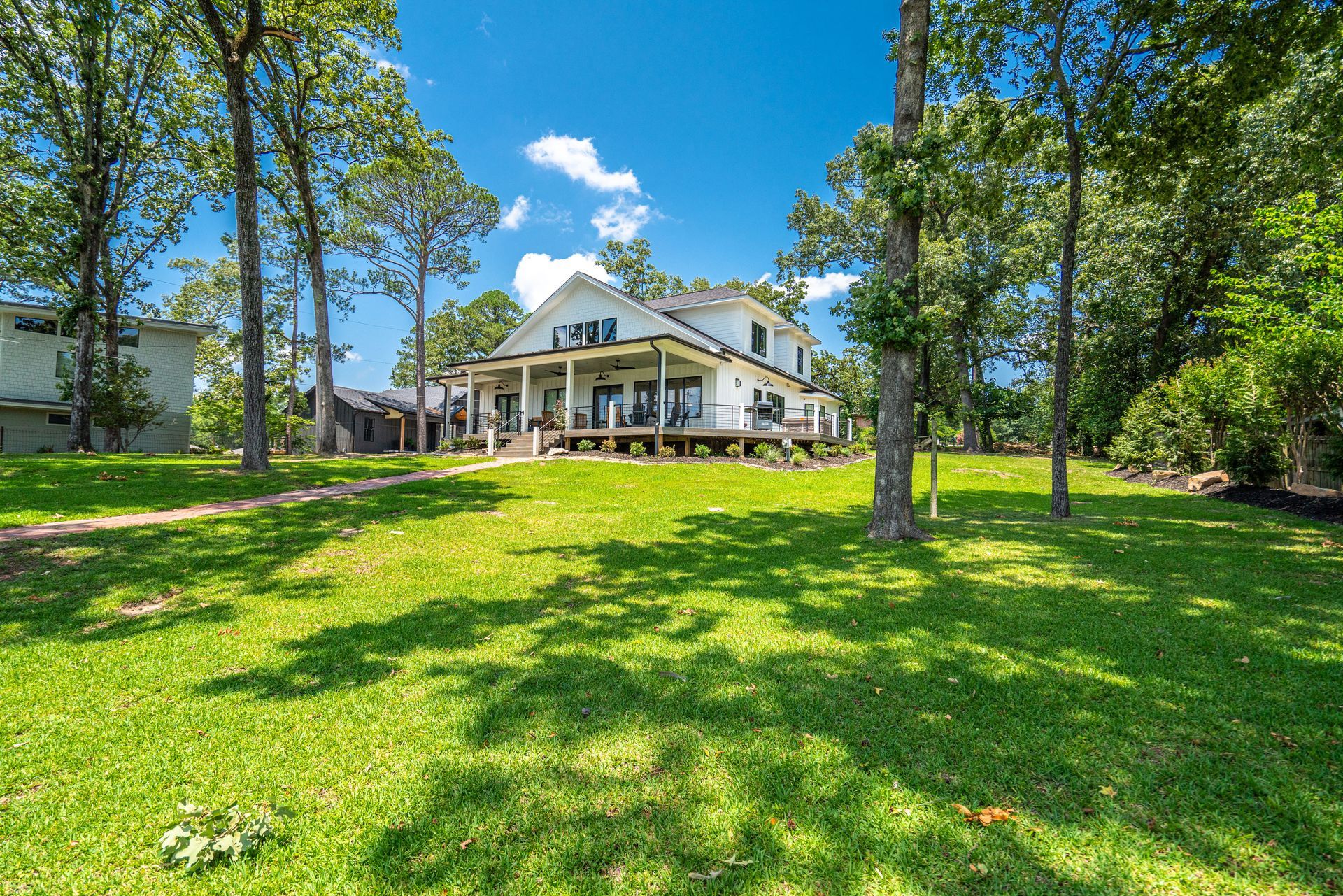 A large white house is sitting on top of a lush green field surrounded by trees.