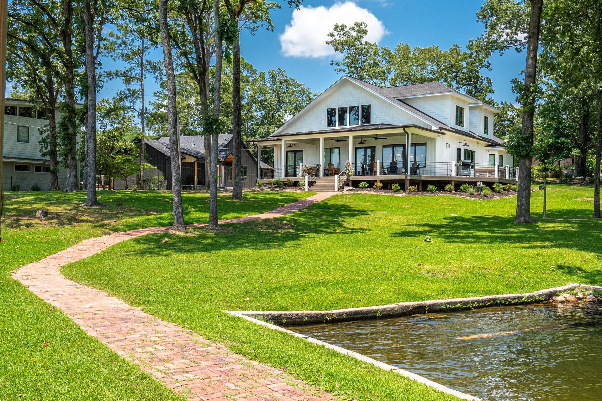 A large white house with a large porch is surrounded by trees and grass.