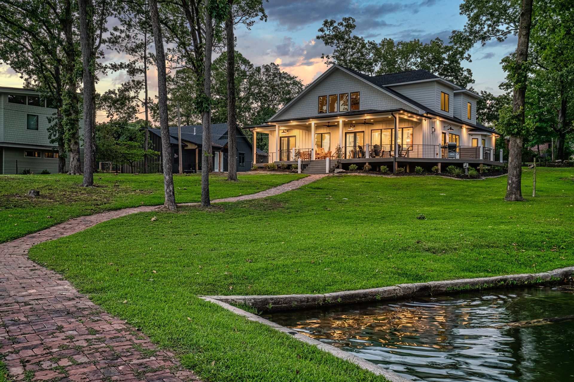 A large white house is sitting on top of a lush green field next to a pond.