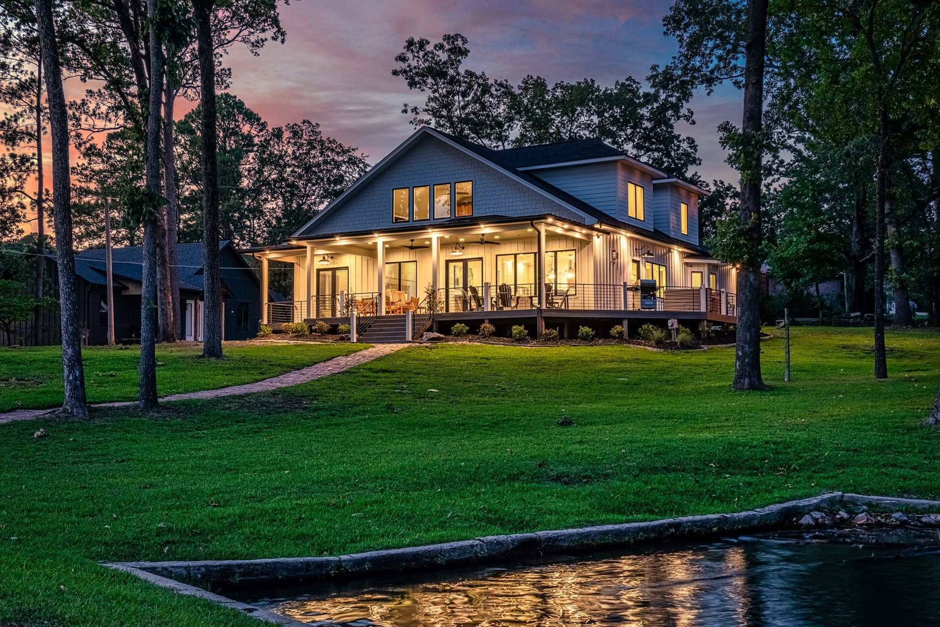 A large house is sitting on top of a lush green field next to a body of water.