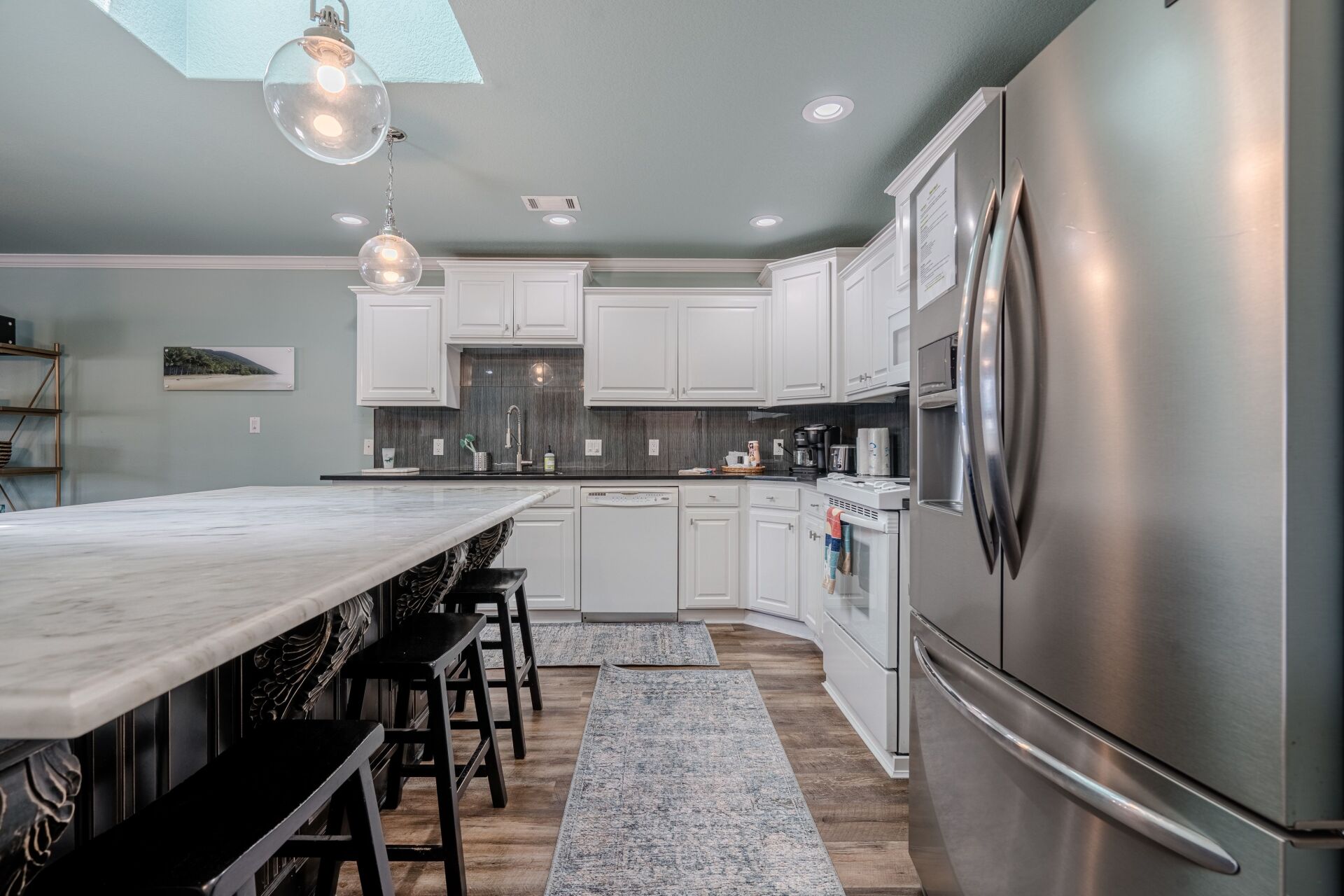 A kitchen with white cabinets , stainless steel appliances and a large island.