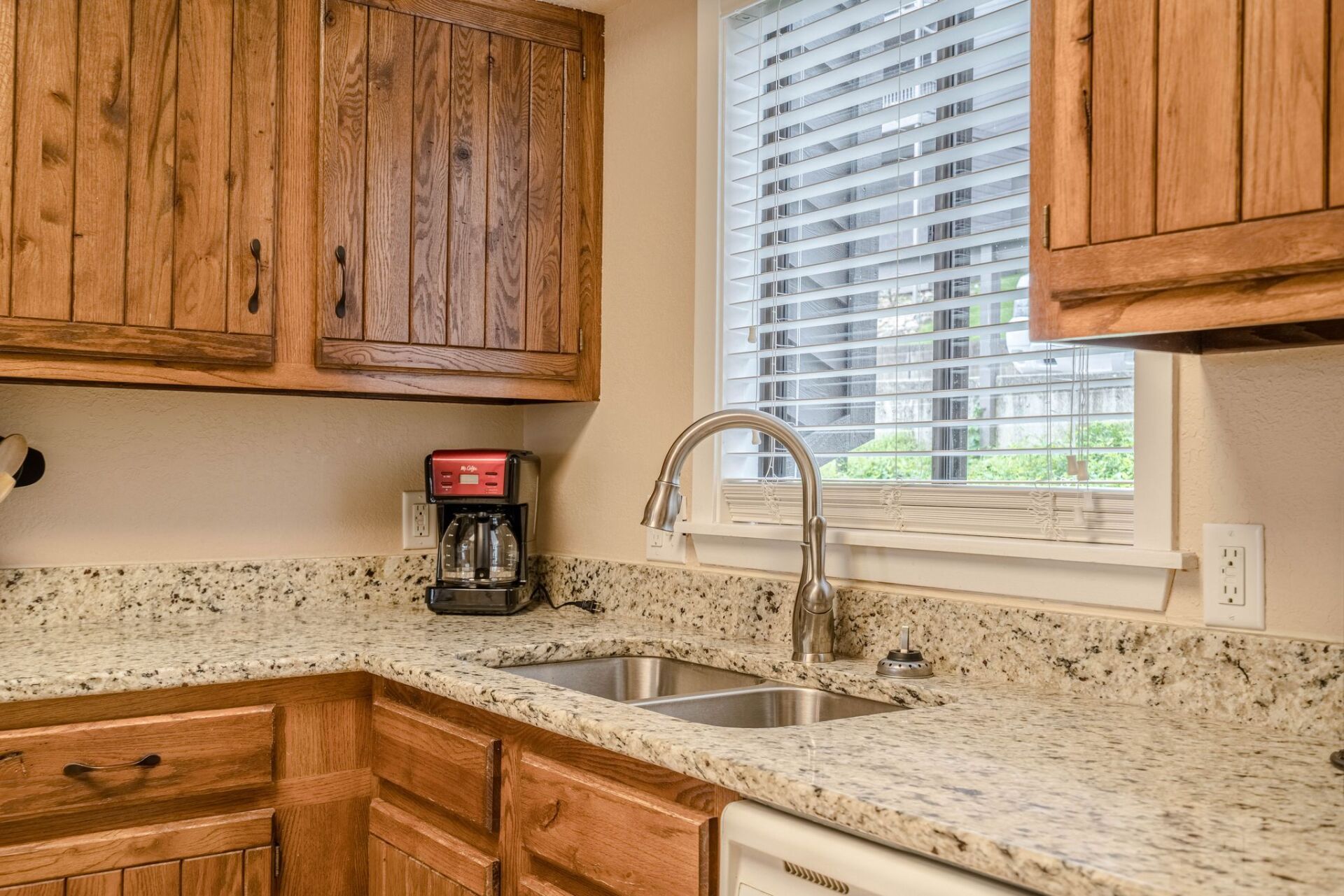 A kitchen with two sinks , granite counter tops , wooden cabinets and a window.