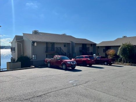 Apartment complex near water with red pickup trucks parked in front on a sunny day.
