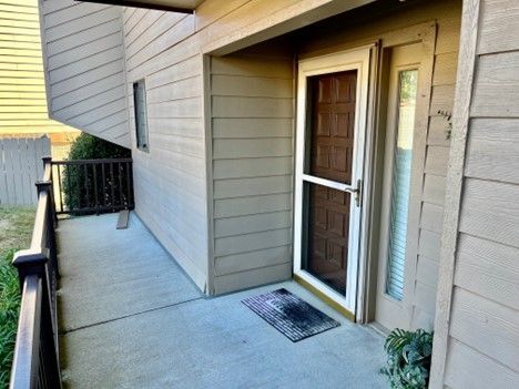 Exterior of a tan apartment with a concrete porch, screen door, and a welcome mat.