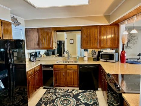 U-shaped kitchen with wood cabinets, black appliances, light countertops, and floral rug.