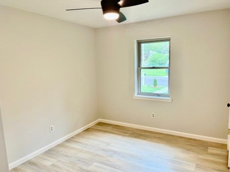 An empty bedroom with a ceiling fan and a window.