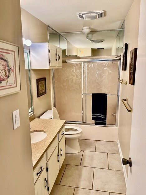 Bathroom with beige walls, tile floor, vanity, toilet, mirrored wall, and shower.