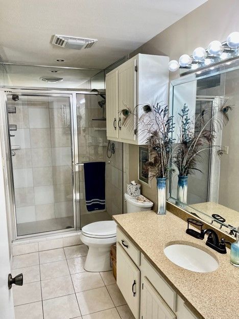 Bathroom with a glass shower, toilet, vanity, and tan countertops. Cream-colored cabinets and light tiles.