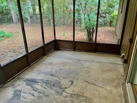 An empty screened in porch with a concrete floor and trees in the background.
