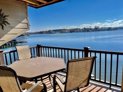 Patio overlooking a blue lake with table and chairs. Sunny day, distant buildings.