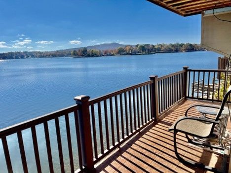 Lake view from a brown wooden deck with two chairs, overlooking a lake and distant mountain under a blue sky.