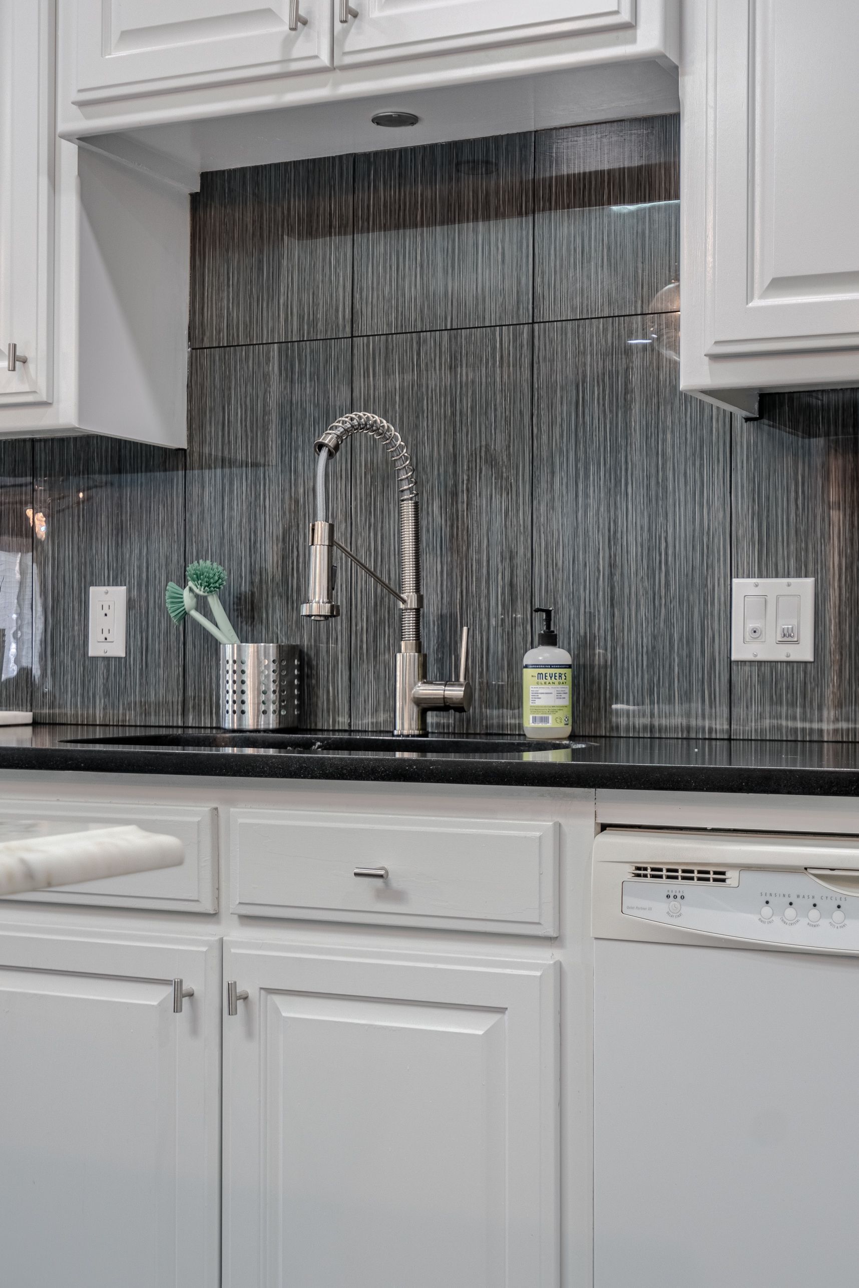A kitchen with white cabinets , a sink , and a dishwasher.