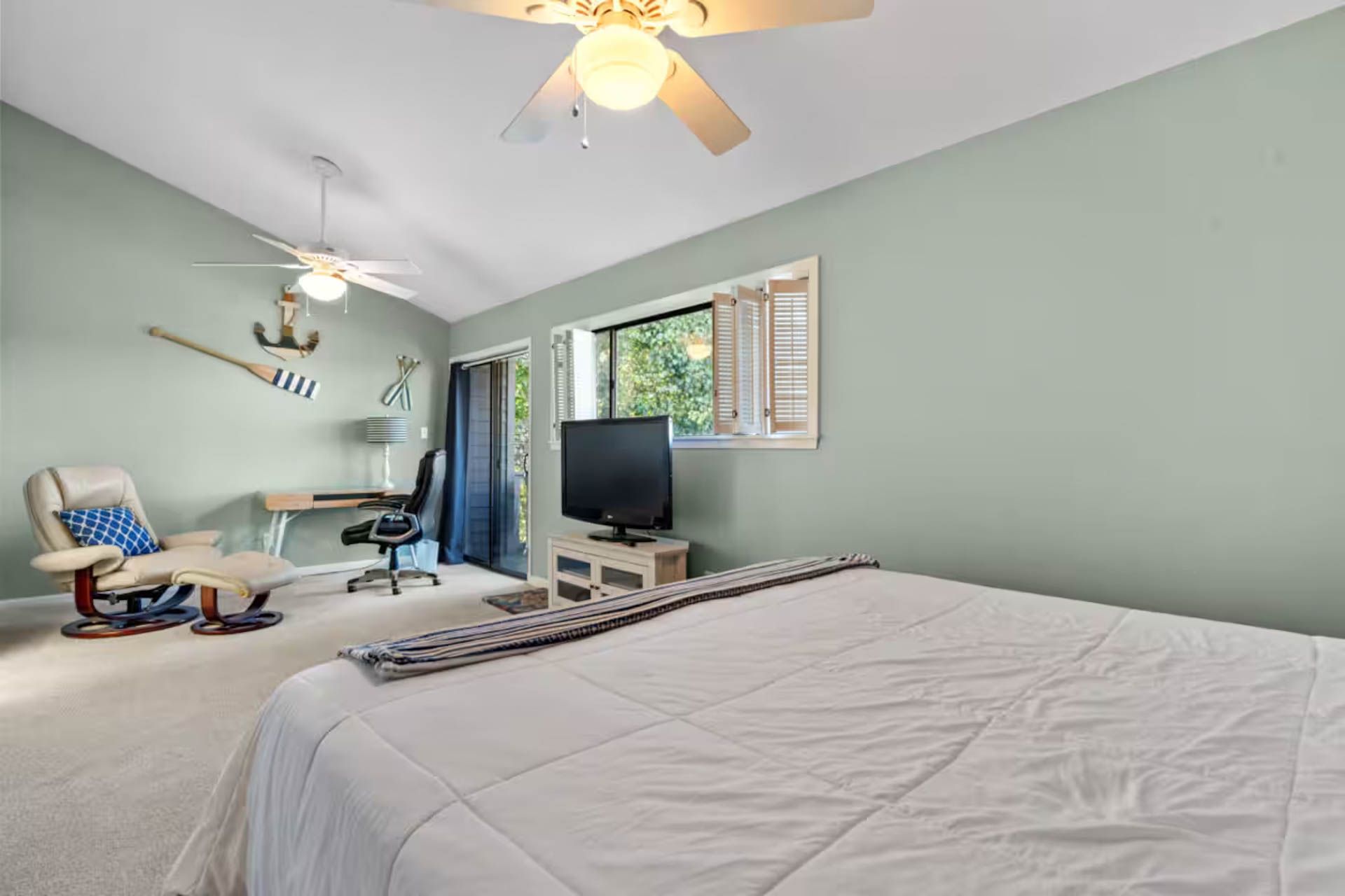 Bedroom with a vaulted ceiling, painted light green. A bed, chair, desk, and TV are present. Two ceiling fans.