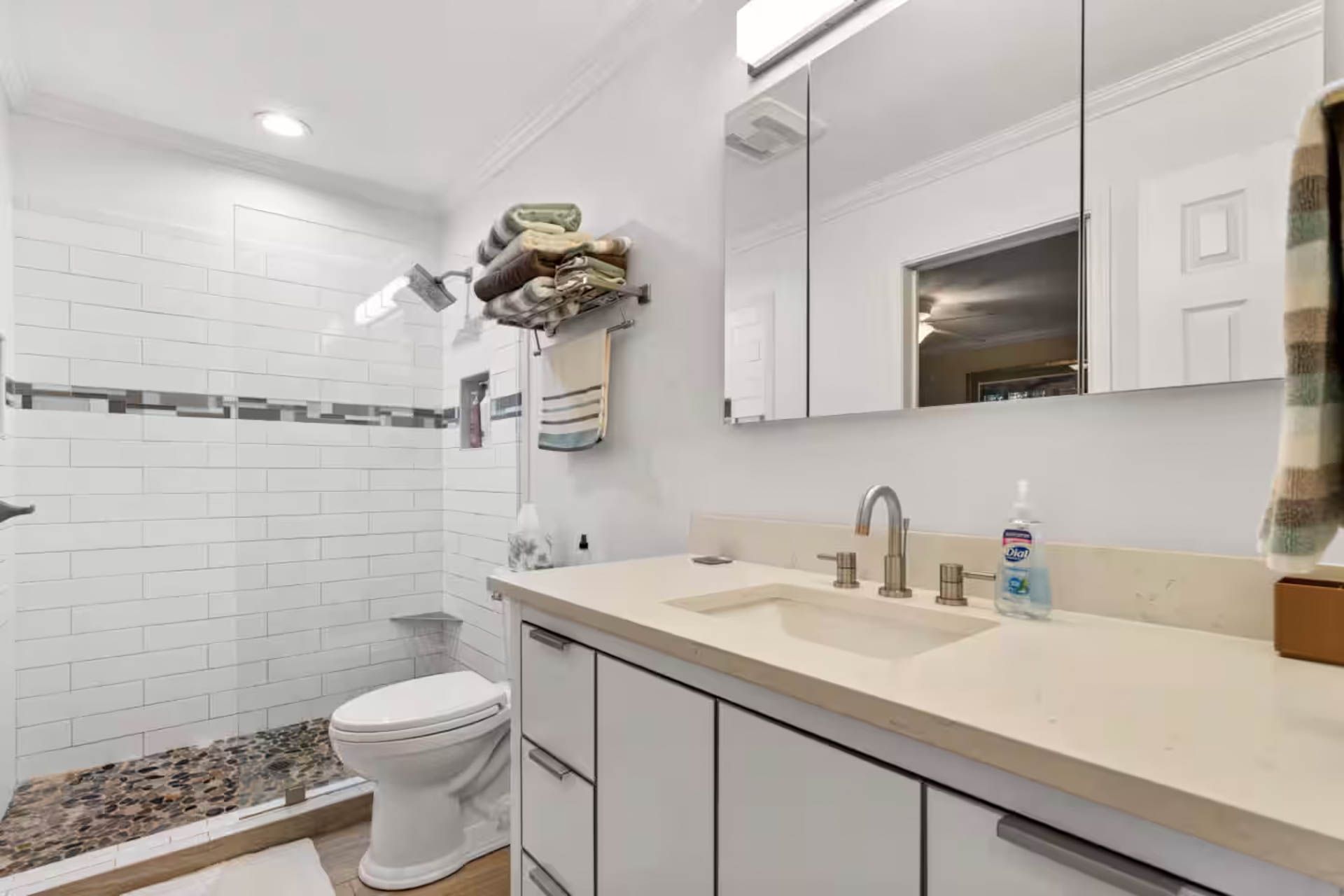 Bathroom with white cabinets, shower, toilet, and sink. Beige countertop, towels hanging, mirror.