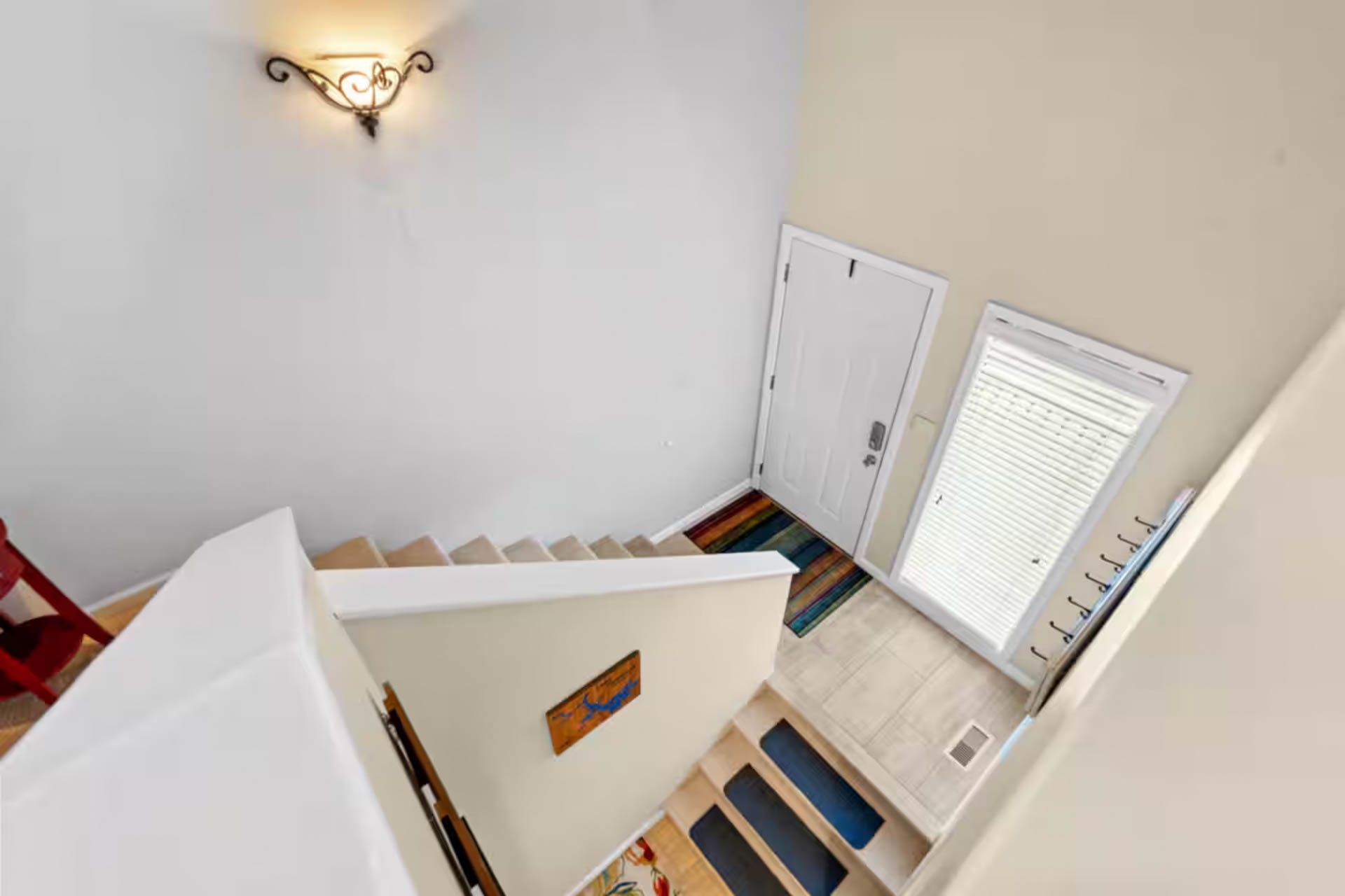 Staircase leading down to a front door and window. Beige walls and cream-colored stairs.