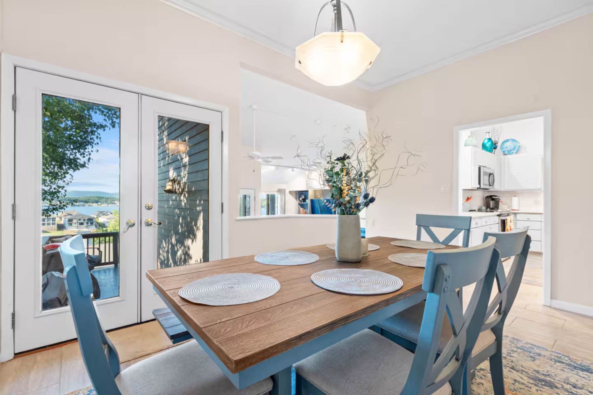Dining room with wooden table, blue chairs, white French doors, and a view.